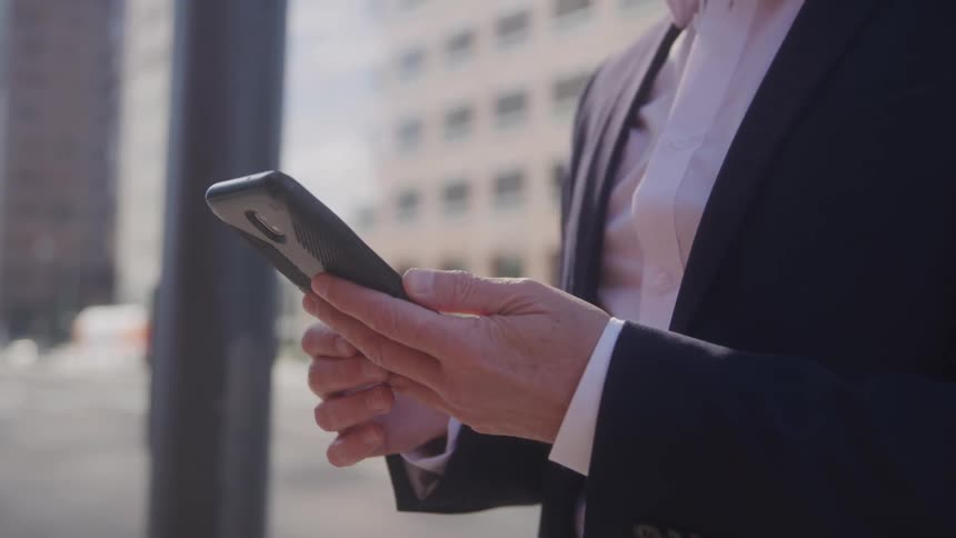 A man in a suit checks his smartphone while standing outdoors in a city environment