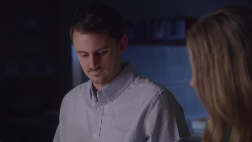 Two colleagues sit side by side in a dimly lit office reviewing blueprints together late at night