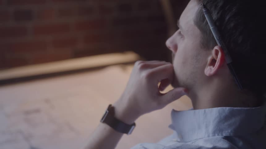A man in deep thought sits with a document in front of him and a pen tucked behind his ear