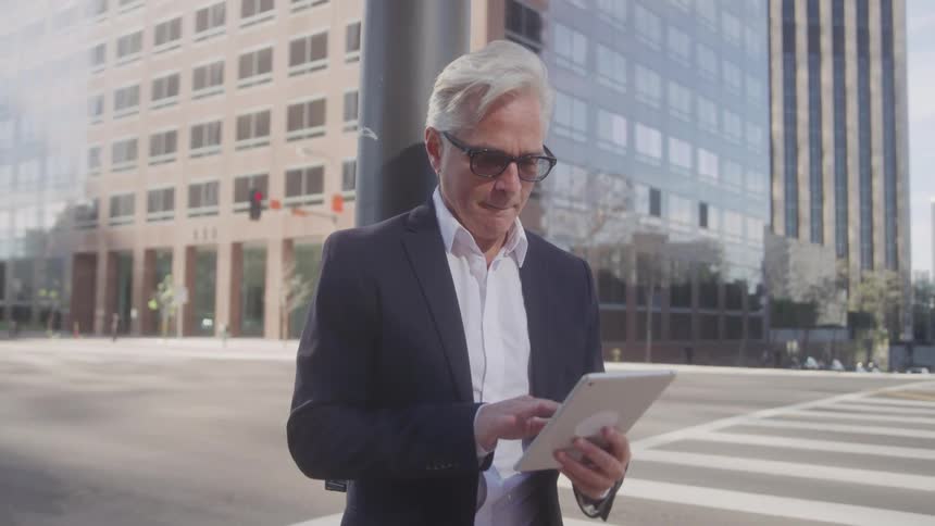 The man is using his tablet on the city street corner