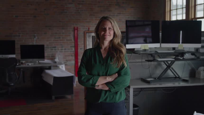 A confident woman stands with arms crossed in a modern office smiling calmly at the camera