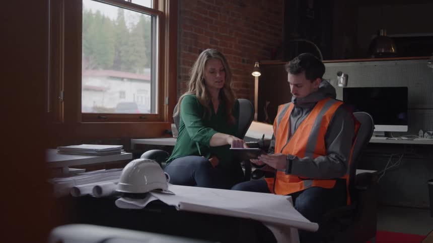 Man and a woman sitting in an office area discussing in front of a tablet