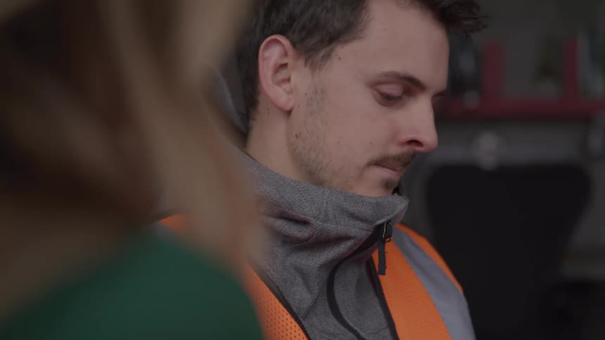A bearded man in glasses looks concerned while speaking to a woman who listens attentively