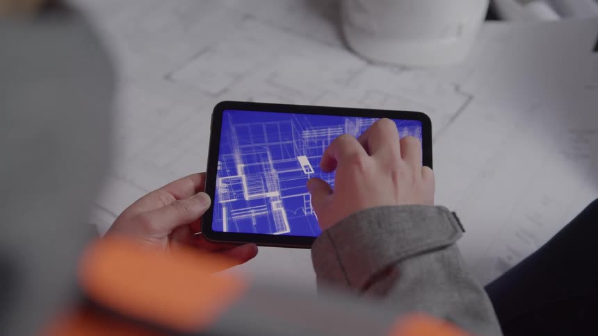 A person points to a digital blueprint displayed on a tablet while another person uses the tablet by touch