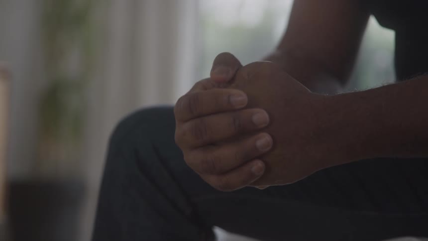 A person sits with their hands clasped in front of them conveying a quiet contemplative posture