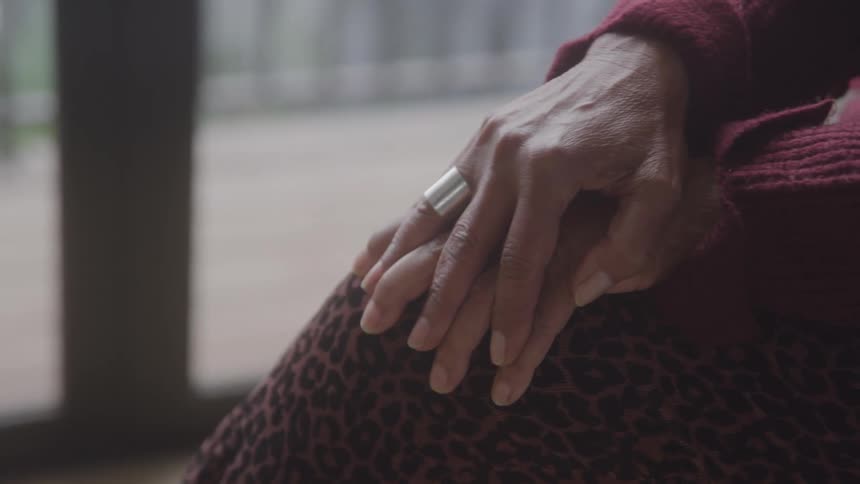 Close up of a black womans hands as she rubs her knees while sitting with her legs crossed in a room during daytime