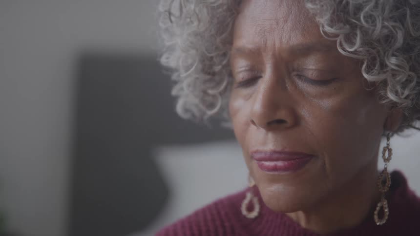 Close up portrait of an elderly black woman contemplating while sitting in a room during daytime