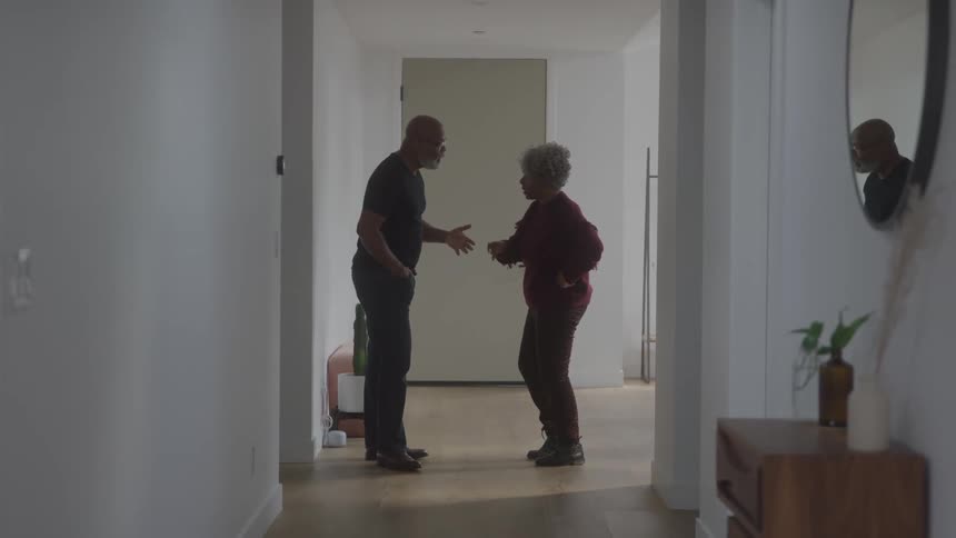 A man and woman stand in a hallway having an animated dicussion