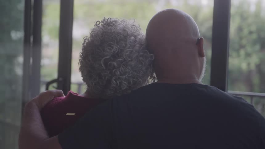 A older man affectionately puts his arm around the should of his female companion