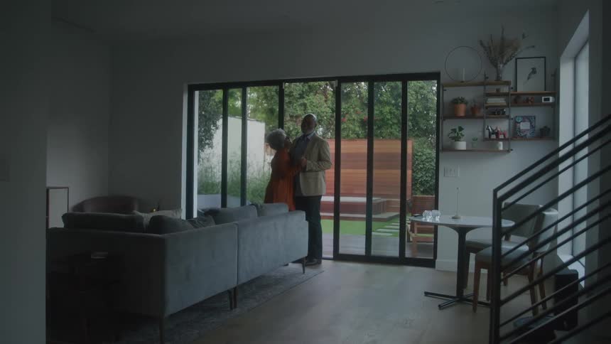Elderly couple dances in place near sliding glass doors in their living room