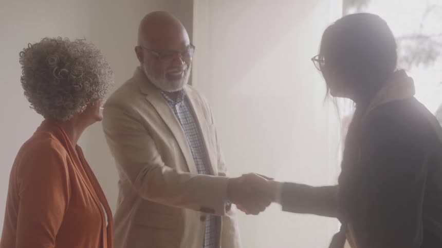 Realtor shakes hands with an elderly couple while standing near an open door during the daytime