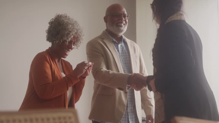 This video shows three individuals interacting in what appears to be a professional or business setting an older black couple the woman with curly grey hair and the man with a beard and glasses are engaging with another person whose back is mostly to t