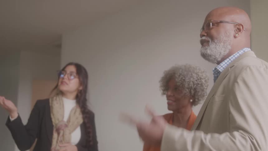 A cheerful older couple discusses something with a smiling real estate agent while touring a property