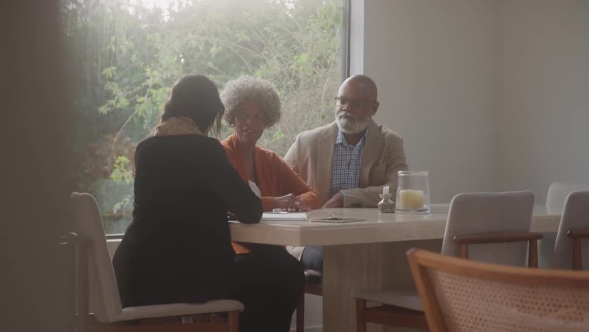 Three people sitting at a table during the day talking to each other