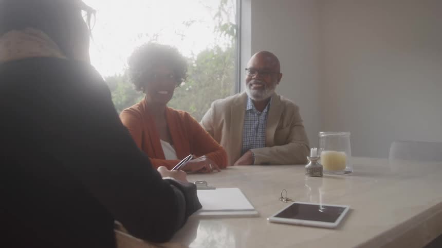 An older couple engages in a friendly discussion across a table from a professional bathed in natural light from a nearby window