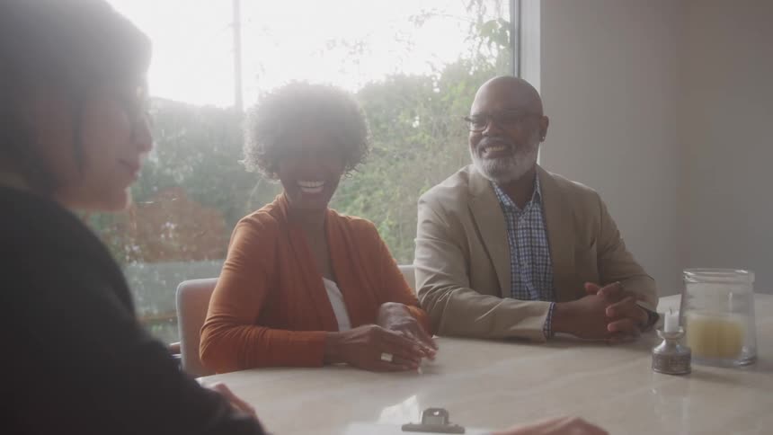 A smiling black couple shakes hands with a professional across a desk