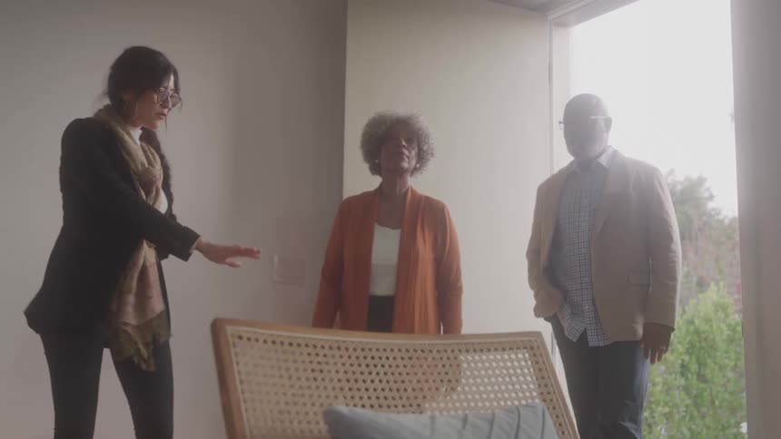 A woman ushers an older couple into an apartment unit and shows them around it