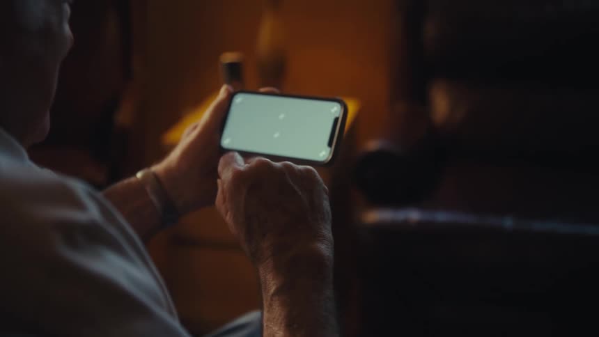 Elderly man smiles while waving at his smartphone during a video call