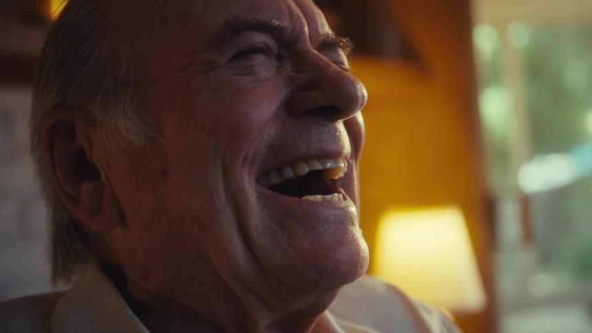 A joyful elderly man is engrossed in his phone illuminated by a warm glow