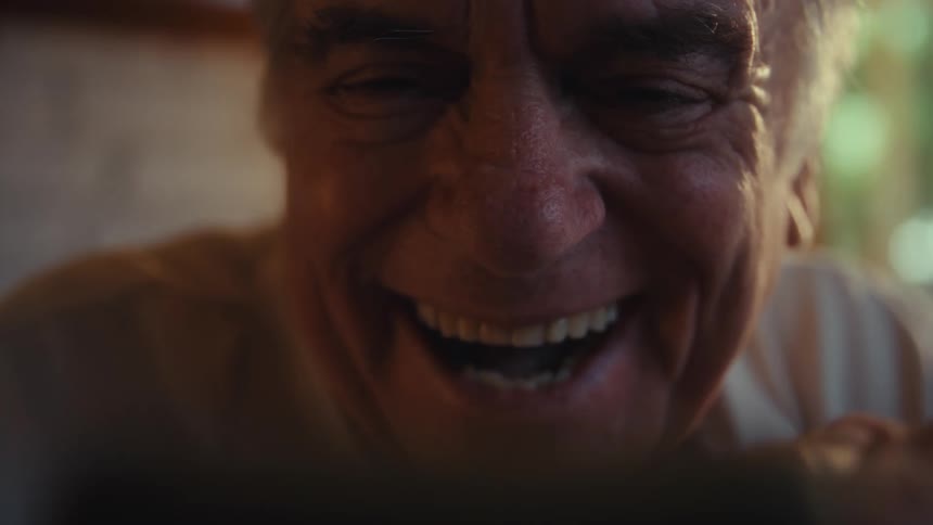 Elderly man sitting in an indoor space inside laughing
