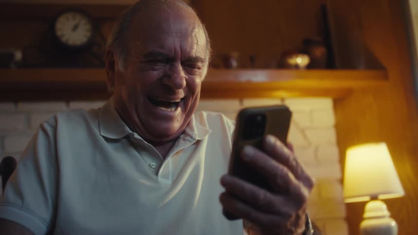 Elderly man sitting and laughing while watching on a smartphone