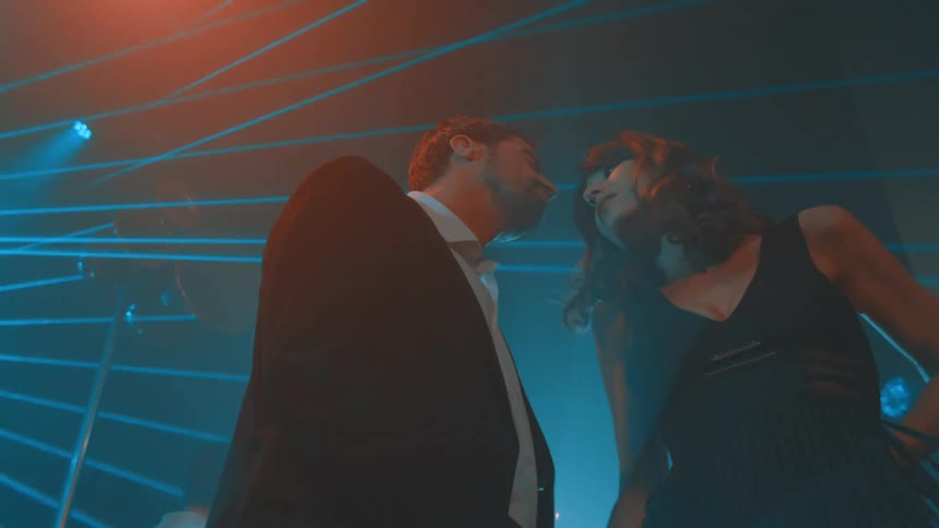 A stylish couple shares an intimate dancing joyful moment under blue laser lights at a lively nightclub