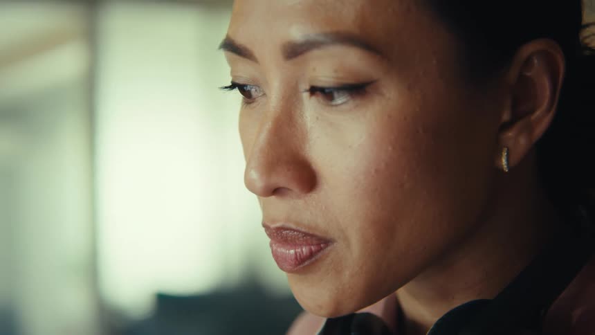 Woman sits indoors viewing a computer while its screen is reflected in her eyes
