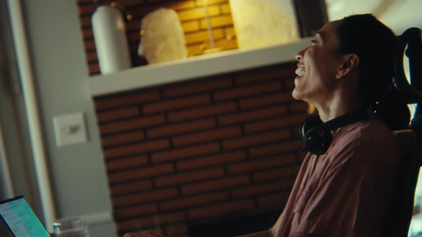 A woman sitting in a home office chair using a laptop and laughing a lot