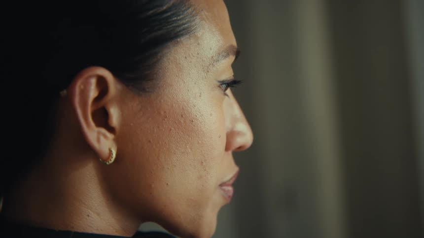 A woman is seen in profile with a composed expression her gaze steady and thoughtful as soft light highlights her face