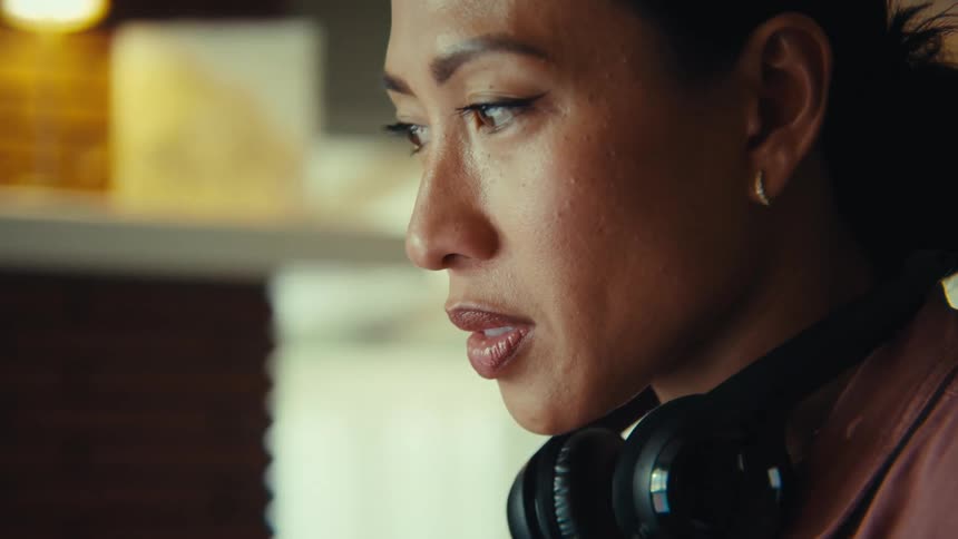 This video features a professional woman likely in her 30s or 40s with dark hair tied back and black headphones around her neck diligently working on her laptop the scene is shot from over her shoulder showing her focused on the screen with a hint o
