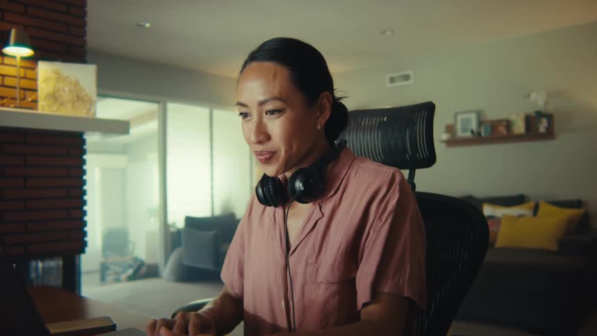 The woman is sitting in an office chair and typing on a laptop