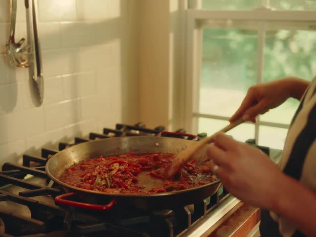The woman is mixing the food on the pan with a wooden spoon