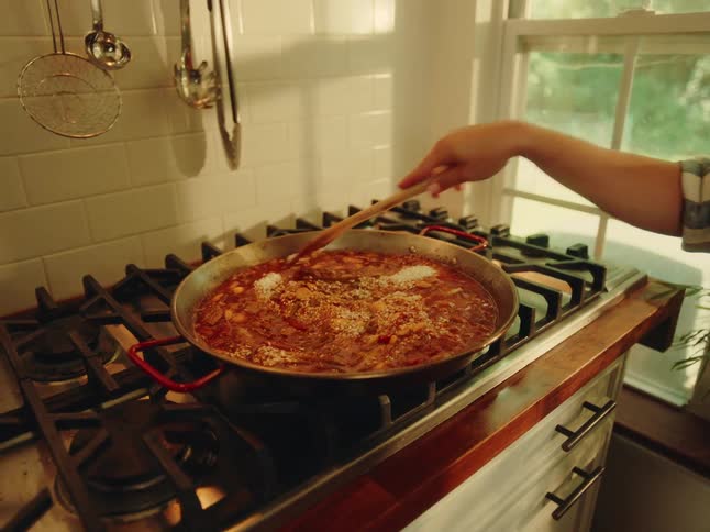 Person with a wooden spoon cooking a red sauce on the stove