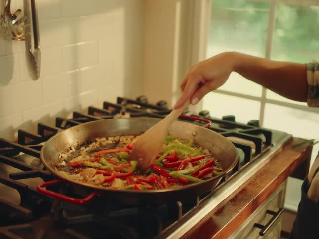 Person with a wooden spoon cooking vegetables in a frying pan