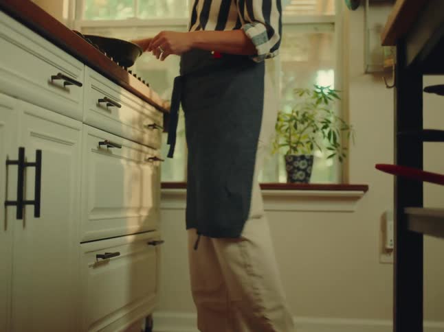 A woman in the kitchen turns food inside a pan on the stove