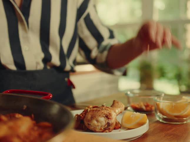 Woman standing in her kitchen seasons a chicken dish while plating it
