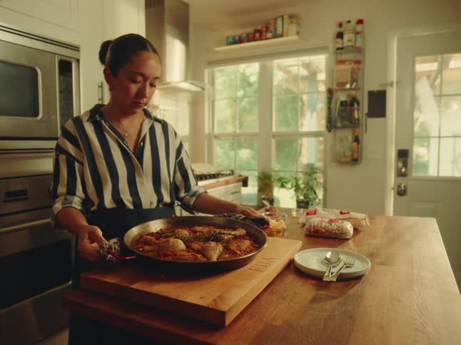 A woman in a kitchen holding a pot with food and placing it on a cutting board