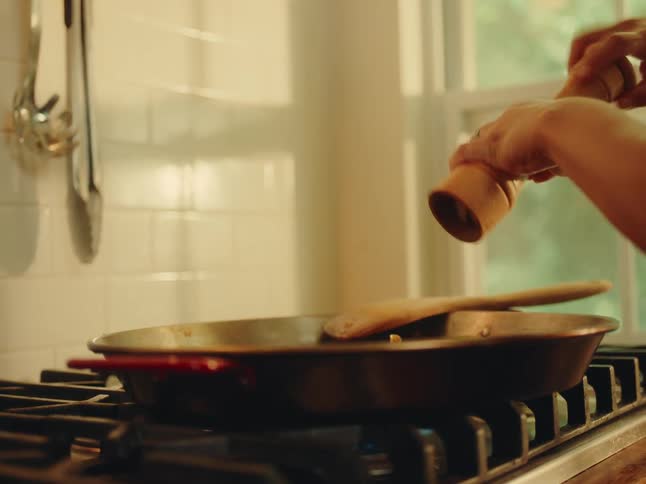 A person grinds spices over a dish cooking on the stove