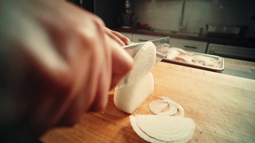 Woman slices a white onion while preparing a chicken dish at home