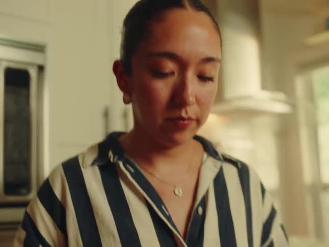 Woman plates a prepared chicken dish while standing in her kitchen during the day