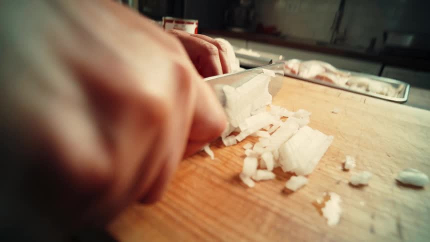 A person cutting an onion with a knife on a cutting board