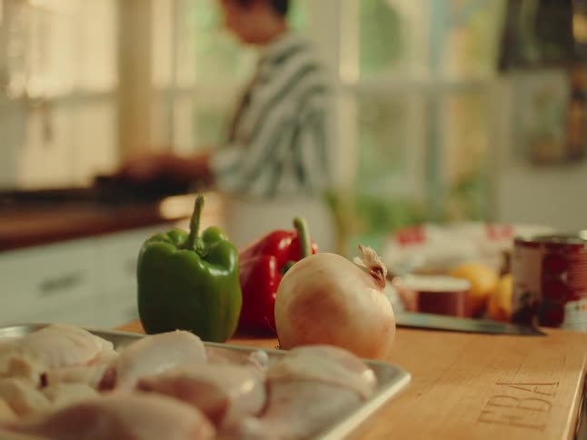 Vegetables and raw chicken prepped as a person cooks in kitchen