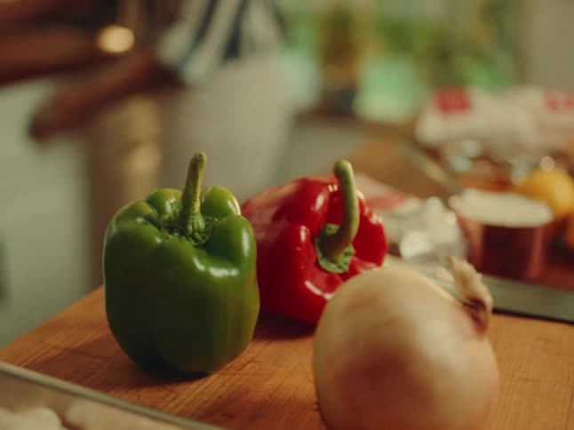 Peppers and onions on a wooden board and a person in the background in the kitchen