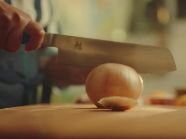 A closeup shot focuses on a person wearing a striped shirt and a dark apron tying the aprons strings around their waist the foreground is blurred showing what appears to be fresh produce on a counter suggesting a cooking or food preparation setting