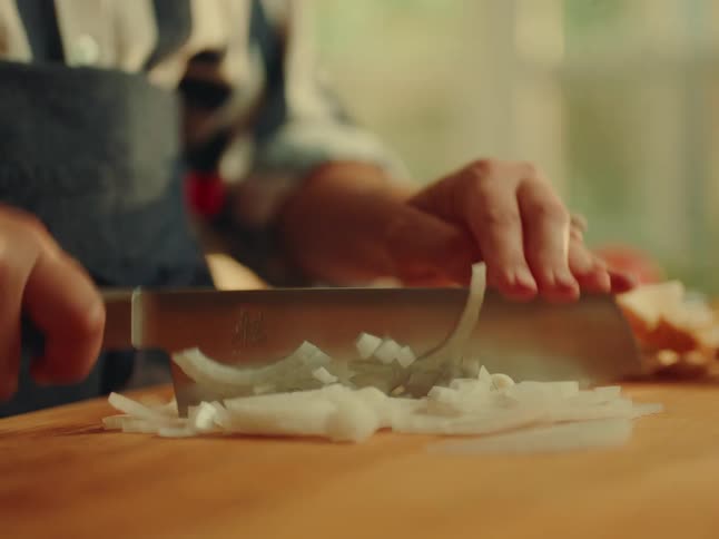 A woman chops onions on a chopping board in the kitchen