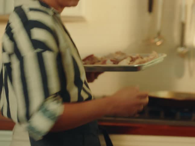 Woman cooking at home prepares to add raw chicken to a pan sitting on a lit burner