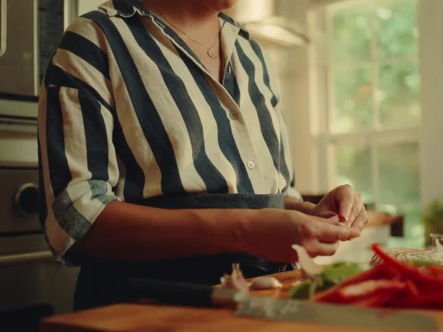 Woman in the kitchen peeling garlic on a wooden cutting board