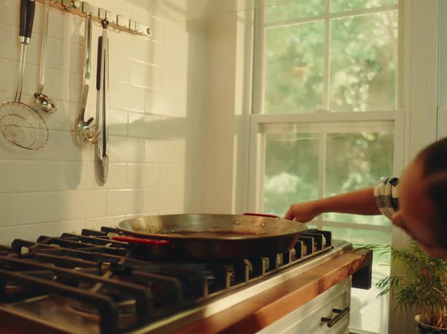 Woman turning on the stove with a frying pan