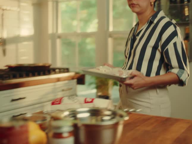 Woman moves around her kitchen gathering ingredients for a chicken recipe during the day