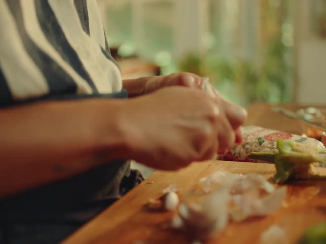 Pair of womans hands peeling garlic on a wooden cutting board